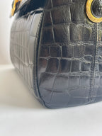 Close-up of a black crocodile-embossed leather handbag corner with gold-tone hardware on a white background.