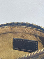 Close-up of the interior of a zippered pouch or bag, showing a tan canvas lining, a black leather brand patch, and a gold-toned zipper.