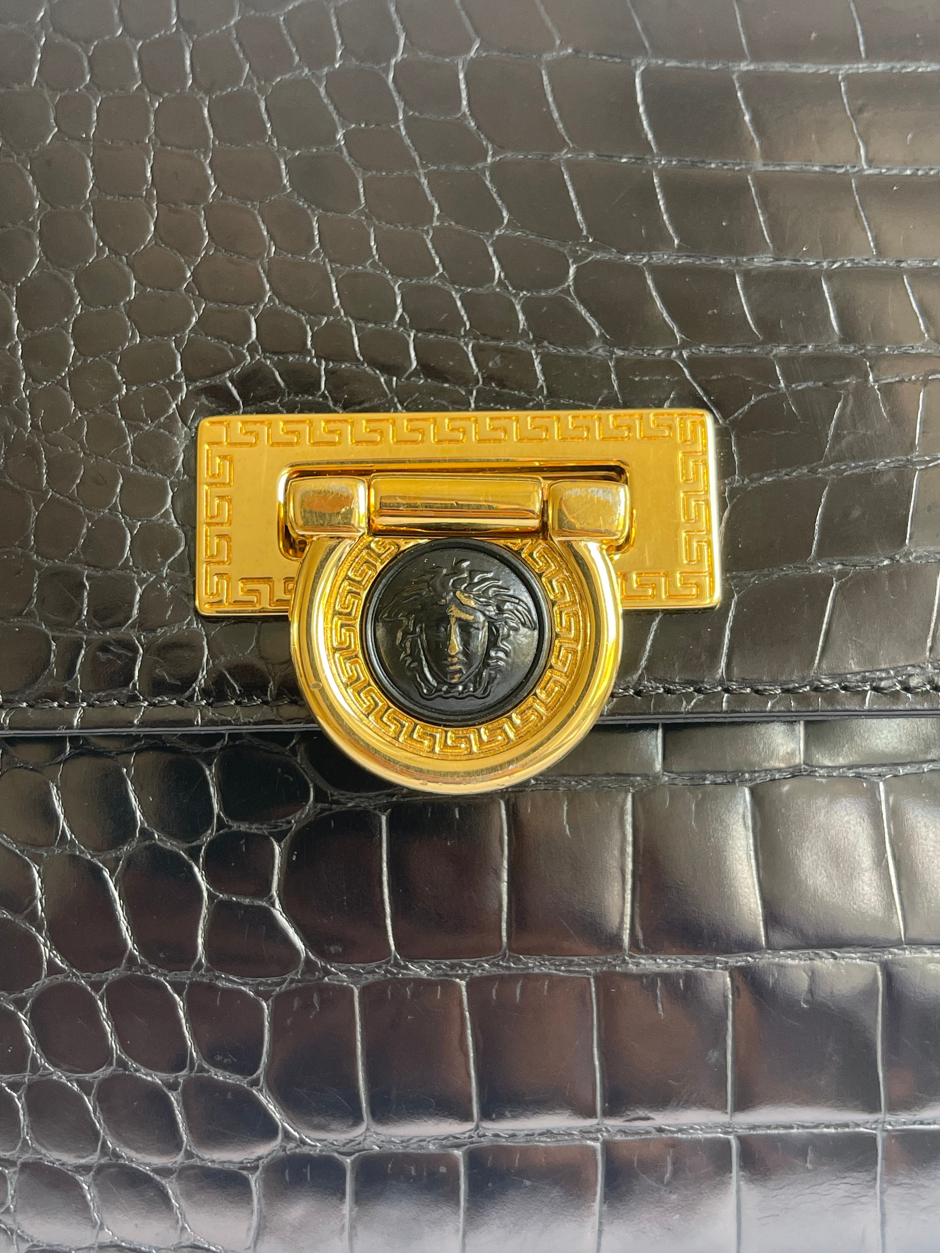 Close-up of a luxury handbag featuring a dark brown crocodile-embossed leather flap and a prominent gold-tone metal clasp with a circular Medusa head emblem.